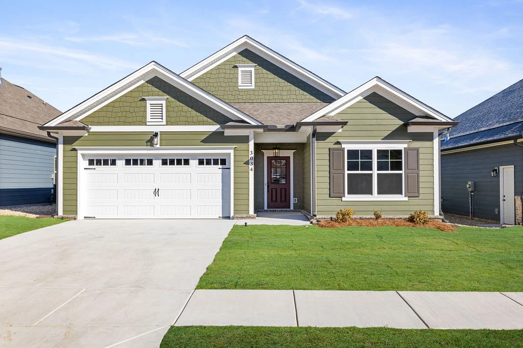 Green craftsman-style home with white garage and driveway by Pratt Home Builders in Chattanooga TN, surrounded by lawns under a blue sky.