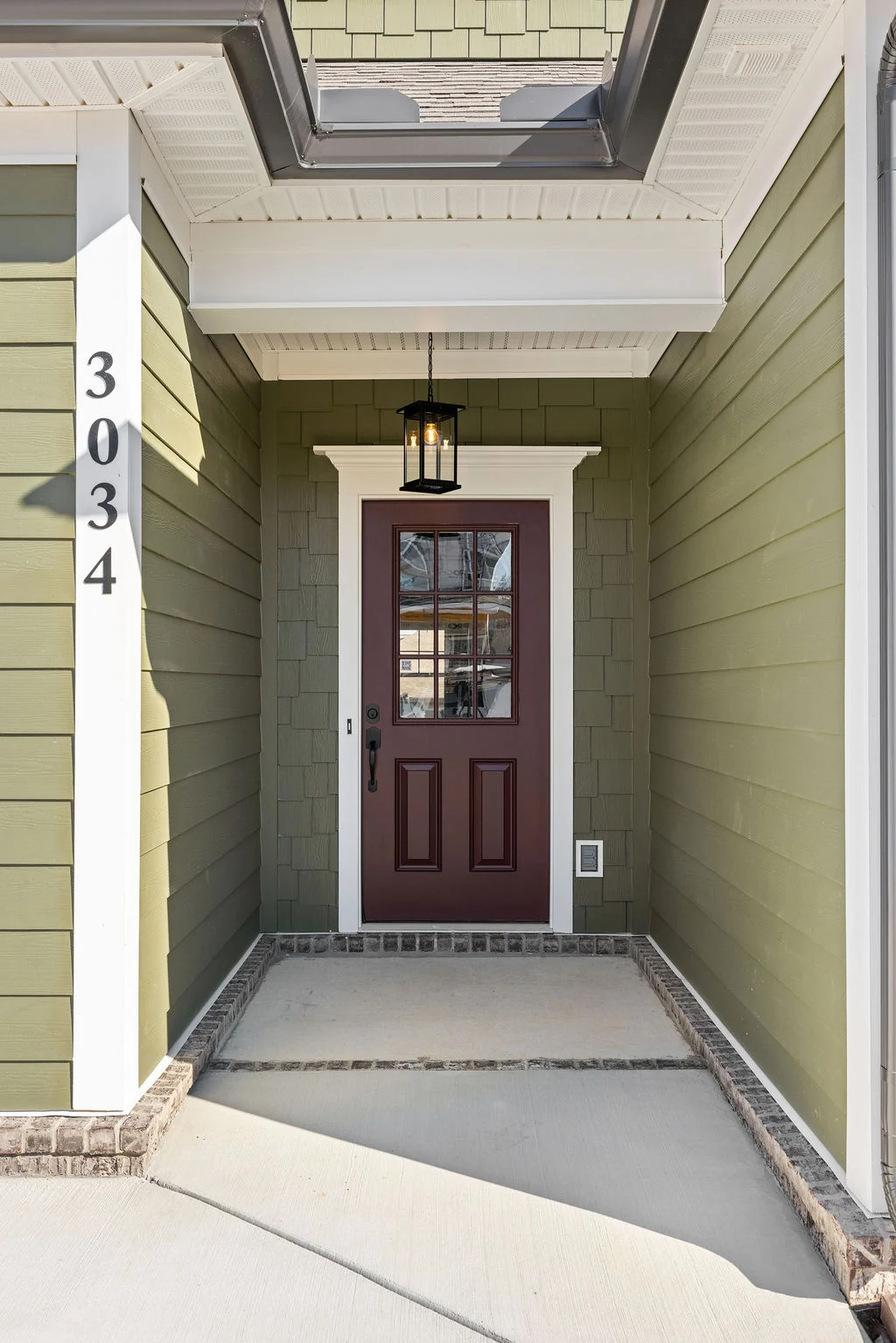 Red door entryway with modern lantern light fixture, olive siding, and address number "3034," designed by Pratt Home Builders in Chattanooga TN.