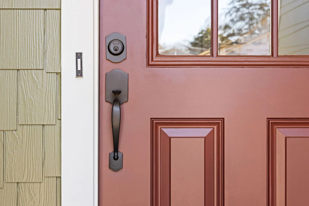 Red front door with a black handle and textured green siding. Features classic style, reportedly by Pratt Home Builders in Chattanooga TN.