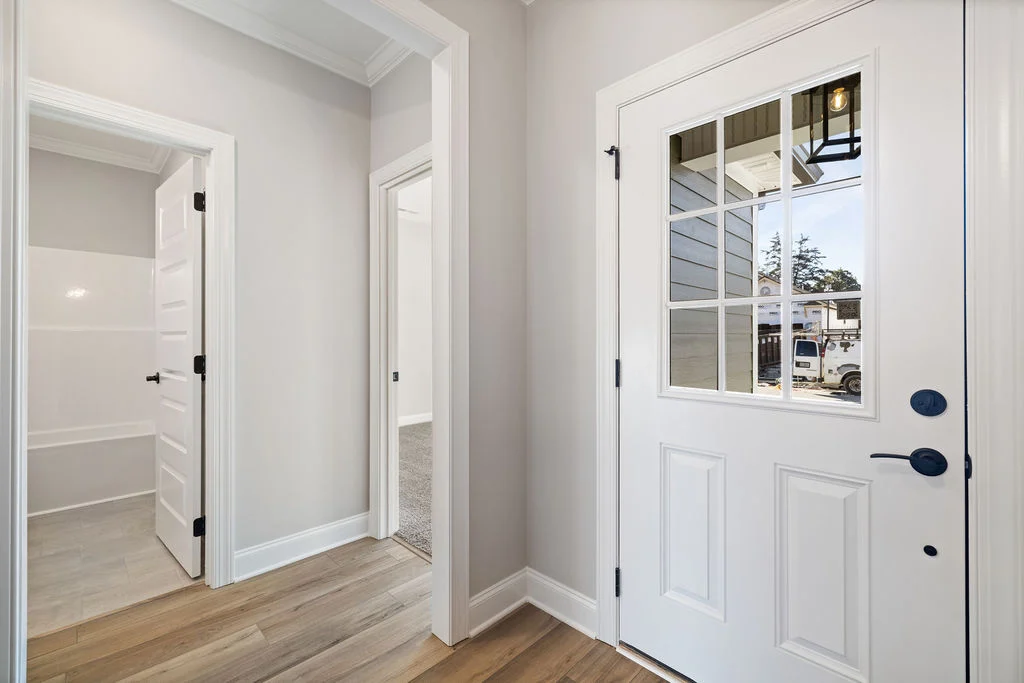 Pratt Home Builders entryway in Chattanooga TN featuring white paneled doors, a windowed door, and light wood flooring.