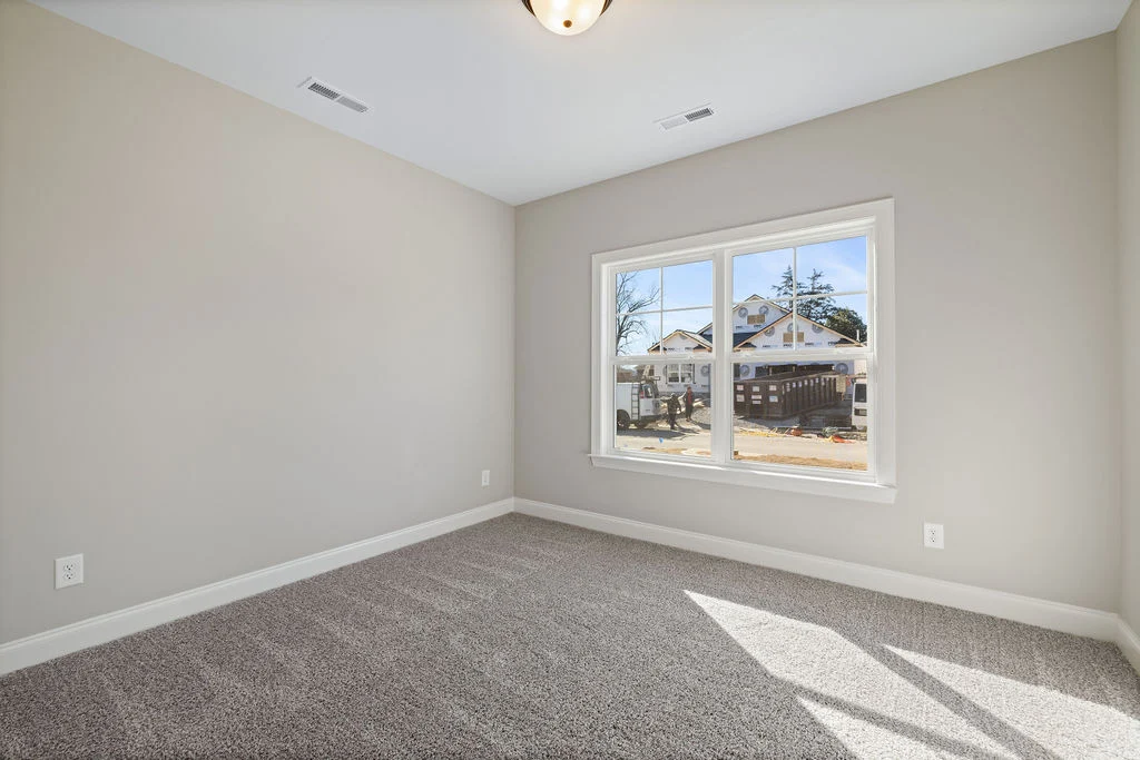 Empty carpeted room with beige walls and large window. Outside, a home construction scene by Pratt Home Builders in Chattanooga TN.