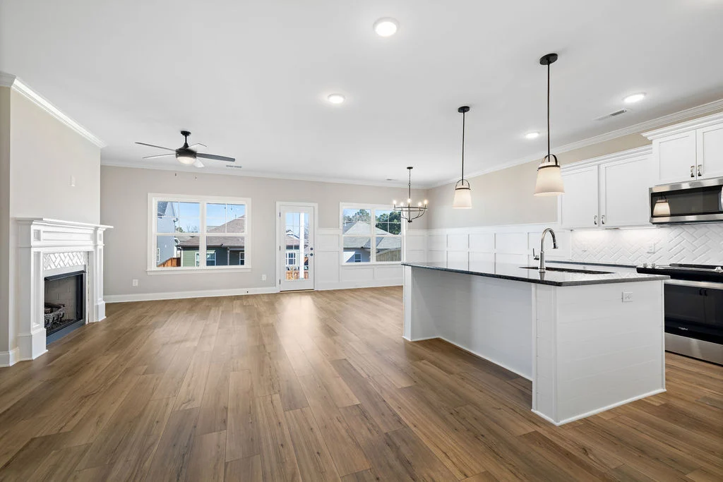 Spacious modern kitchen and living area by Pratt Home Builders in Chattanooga TN, featuring wood flooring, a fireplace, and elegant lighting.
