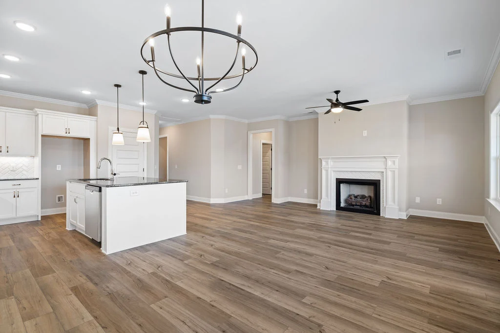 Spacious open-concept kitchen and living area by Pratt Home Builders in Chattanooga TN, featuring hardwood floors, island, chandelier, and fireplace.