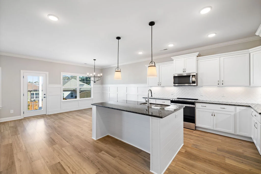 Spacious kitchen and dining area with white cabinets, granite island, hardwood floors. Natural light from wide windows. Pratt Home Builders in Chattan