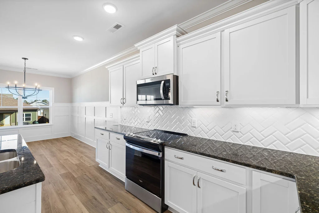 Modern kitchen with white cabinets, herringbone tile backsplash, granite countertops, and chandelier near window by Pratt Home Builders in Chattanooga