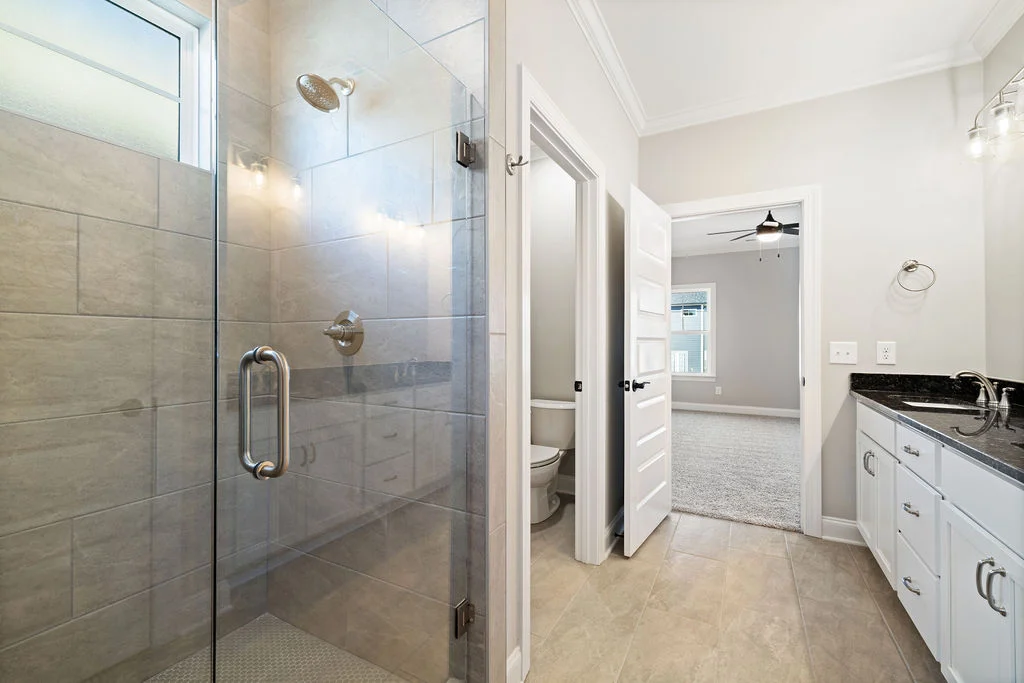 Modern bathroom with glass walk-in shower, dual sinks, and view into a bedroom, designed by Pratt Home Builders in Chattanooga TN.