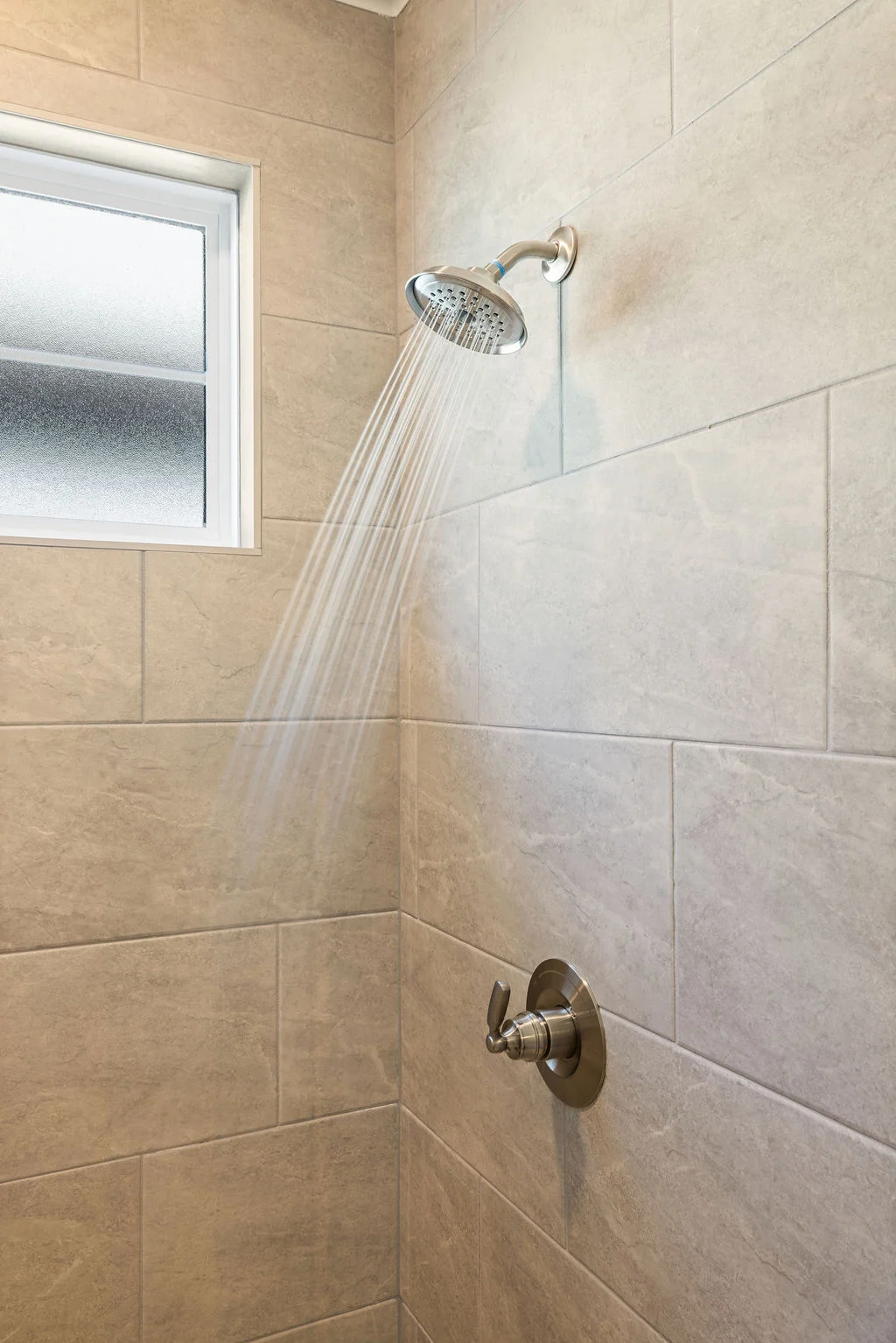 Modern shower with gray tiles, frosted window, and silver fixtures. Design by Pratt Home Builders in Chattanooga TN.