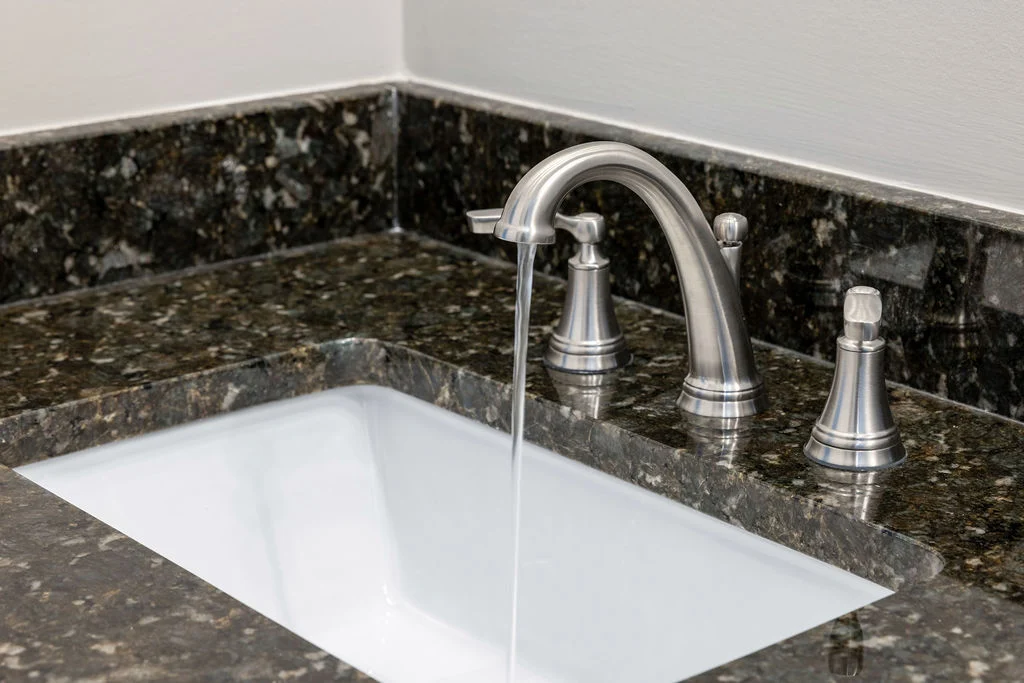 Sleek chrome faucet with water flowing over dark granite countertop, designed by Pratt Home Builders in Cleveland TN.