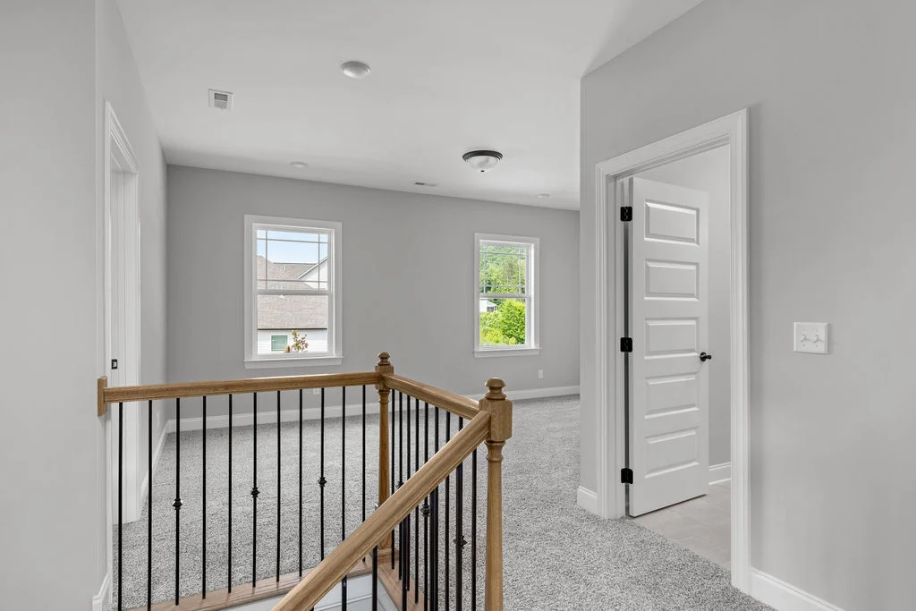 Modern hallway with gray walls, carpeted floors, and wooden railing by Pratt Home Builders in Chattanooga TN, featuring white doors and large windows.