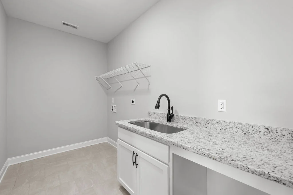 Modern laundry room by Pratt Home Builders in Chattanooga TN, featuring granite countertop, sink, and open shelving.
