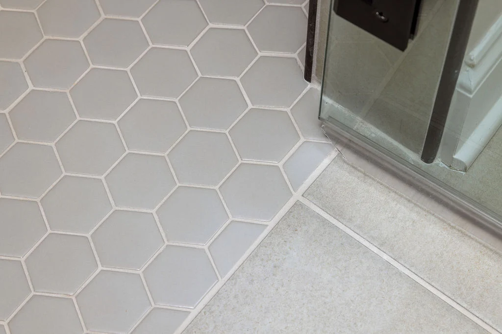 Hexagonal and square tiles meet at a glass shower door, showcasing modern design by Pratt Home Builders in Chattanooga TN.