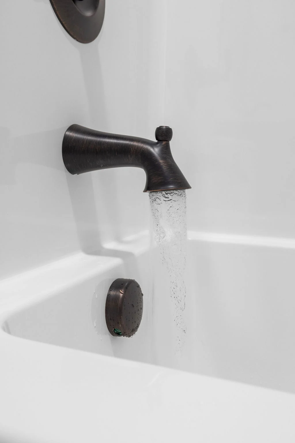 Bronze bathtub faucet with running water in a modern bathroom designed by Pratt Home Builders in Chattanooga TN.