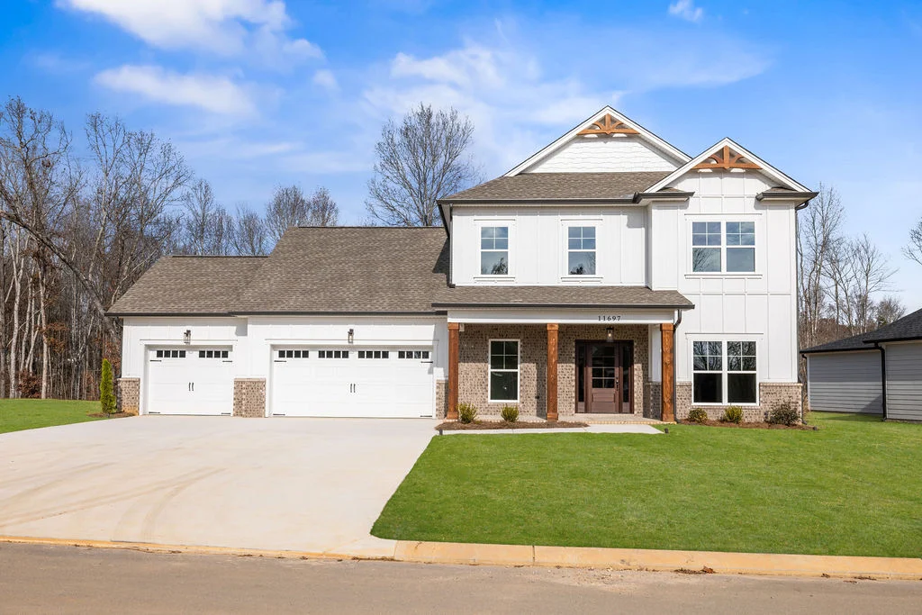 Modern two-story home with three-car garage by Pratt Home Builders in Soddy Daisy, TN, surrounded by trees and a clear blue sky.