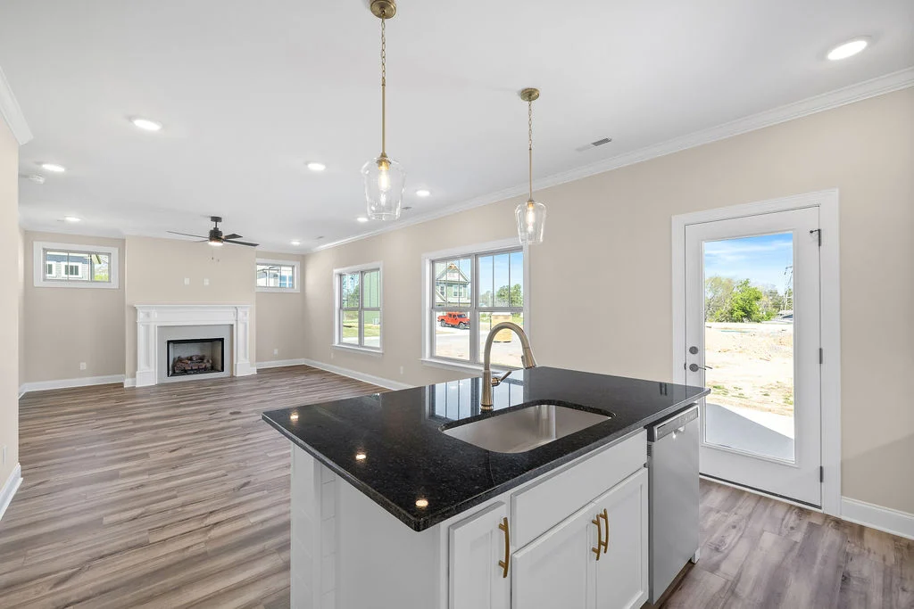 Modern kitchen with sleek island, pendant lights, and adjacent living room with fireplace by Pratt Home Builders in Chattanooga TN.