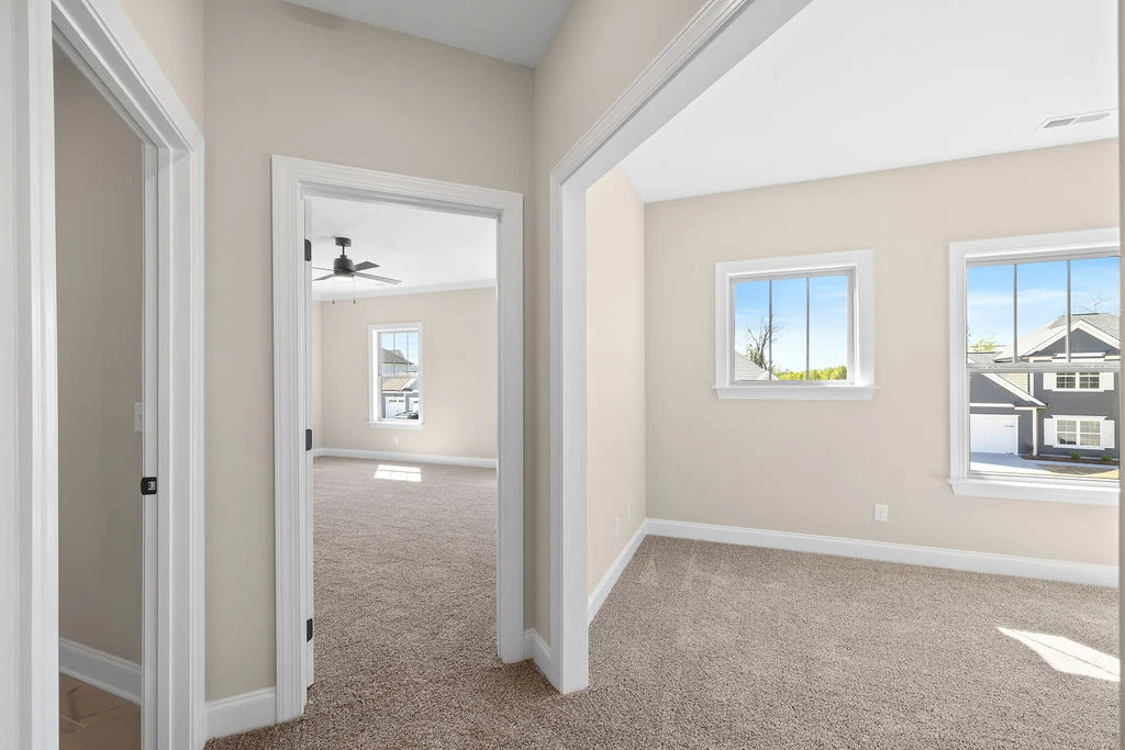 Bright, carpeted room with beige walls, two windows, and adjacent room leading to more space. Pratt Home Builders in Chattanooga TN.