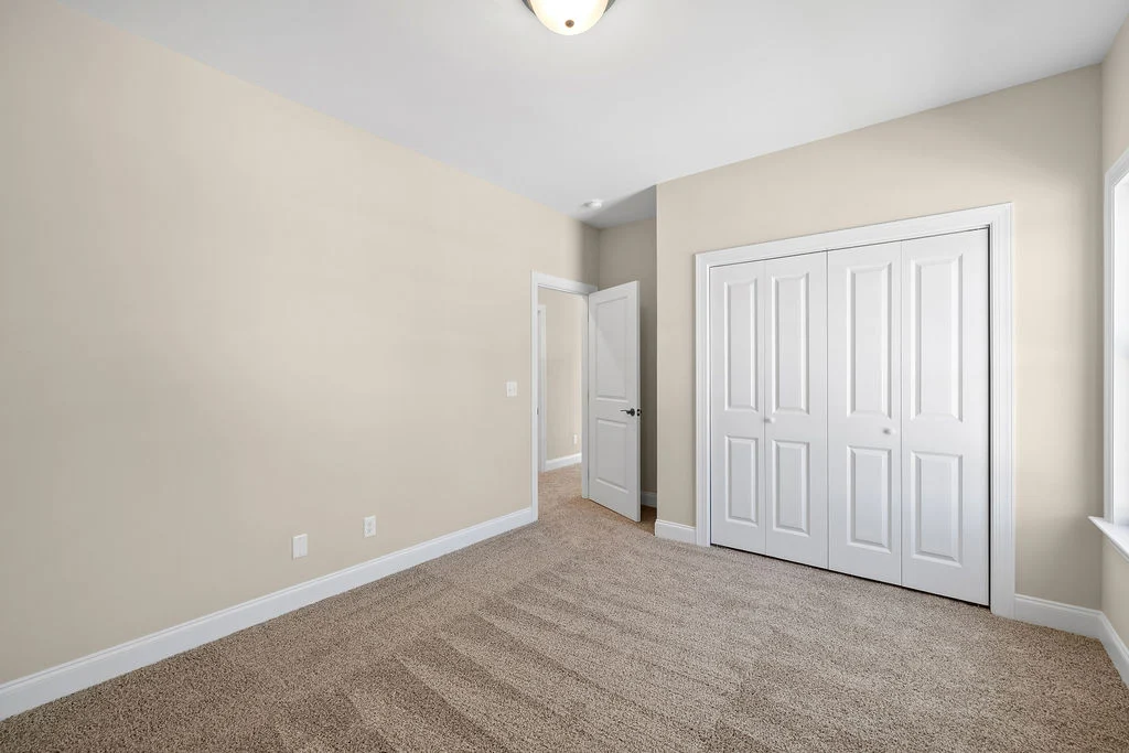 Empty beige room with carpeted floor, white closet doors, an open door, and a ceiling light, built by Pratt Home Builders in Chattanooga TN.