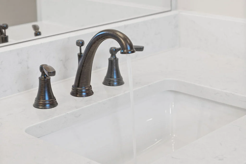 Elegant bronze faucet with flowing water over white marble vanity, crafted by Pratt Home Builders in Chattanooga TN.