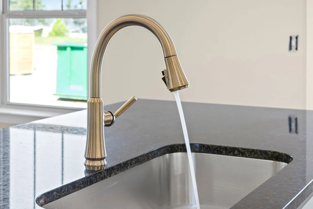 Sleek brass kitchen faucet with running water in a modern, bright kitchen by Pratt Home Builders in Chattanooga TN, featuring granite countertops.