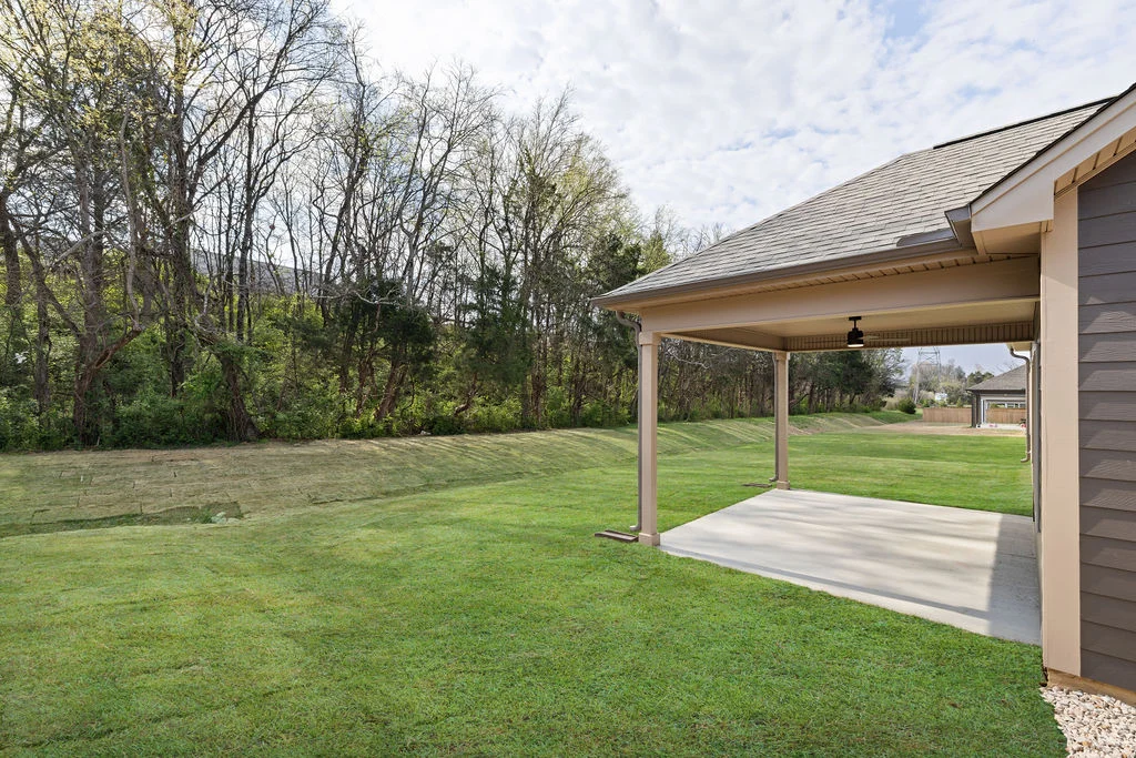 Covered patio with ceiling fan overlooking a lush, grassy backyard and wooded area. Built by Pratt Home Builders in Chattanooga TN.