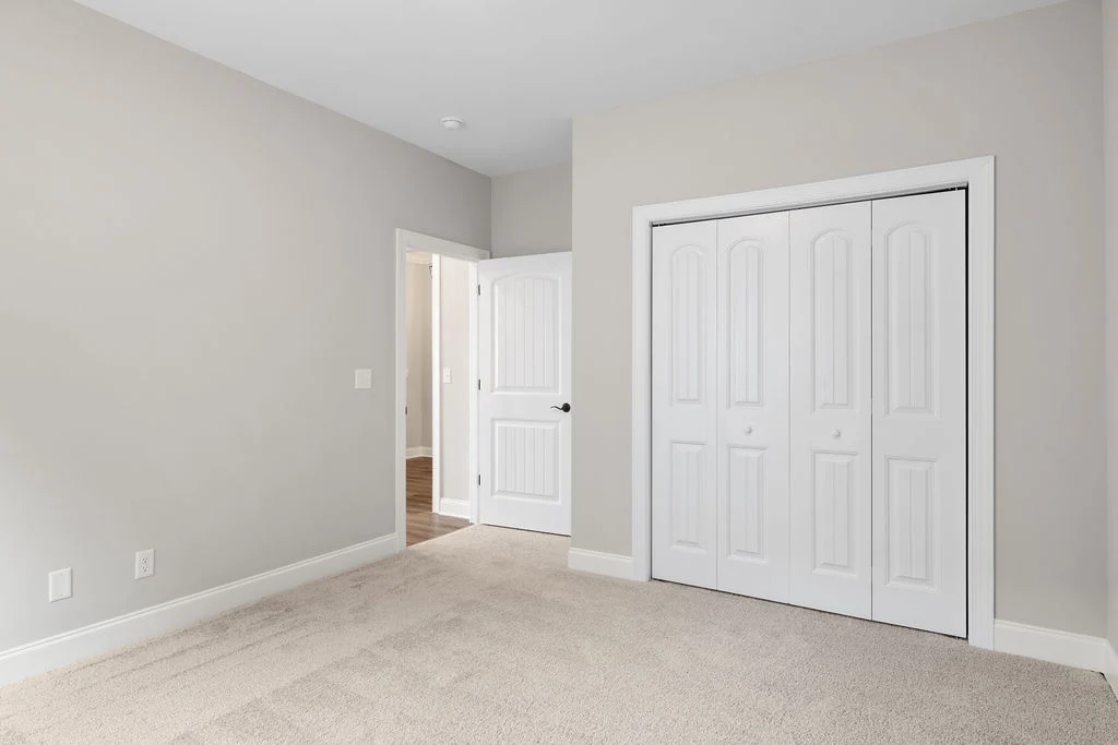 New Home Chattanooga TN. Empty room with beige carpet, light gray walls, a closed closet, and an open door leading to a hallway, designed by Pratt Home Builders.