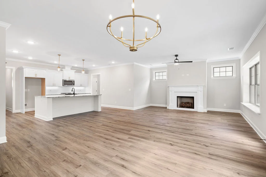 Spacious open-concept living area with hardwood floors, modern kitchen, elegant light fixtures, and a cozy fireplace by Pratt Home Builders in Chattan