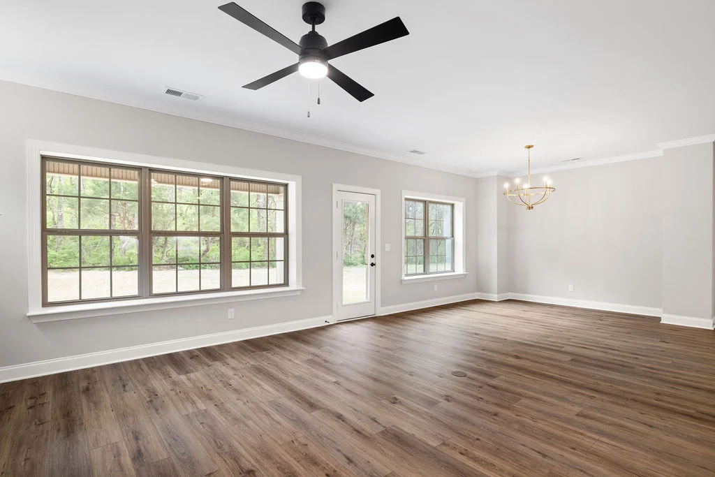 Spacious living room by Pratt Home Builders in Chattanooga, TN; large windows, wood flooring, ceiling fan, and elegant chandelier.