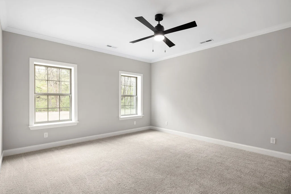 New Home Chattanooga TN. Bright empty room with two windows, beige carpet, gray walls, and ceiling fan by Pratt Home Builders.