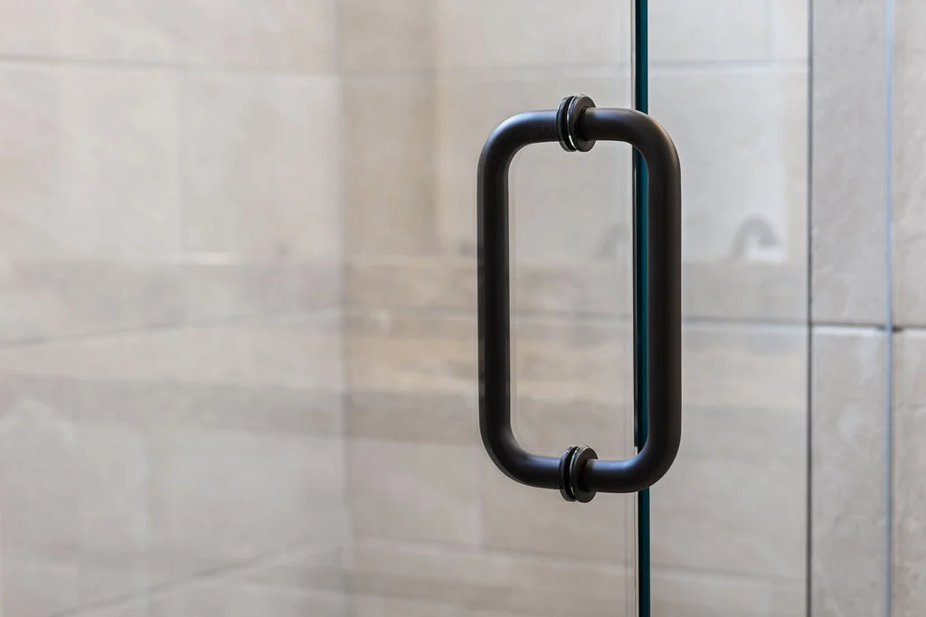 Glass shower door with black metal handle, showcasing sleek design by Pratt Home Builders in Chattanooga TN.