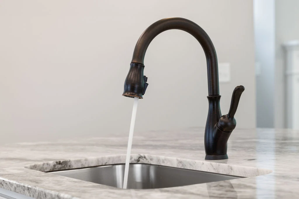 Bronze kitchen faucet on marble countertop, water flowing. Design by Pratt Home Builders in Chattanooga TN.