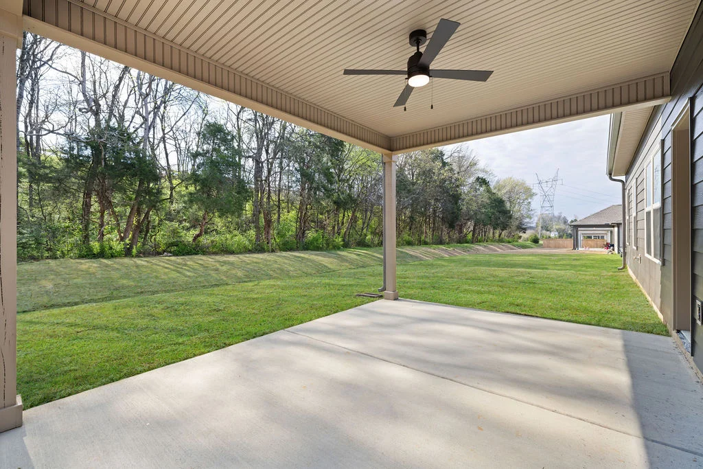 New Home Chattanooga TN. Covered patio with ceiling fan overlooks lush lawn and wooded area, showcasing Pratt Home Builders' backyard design.