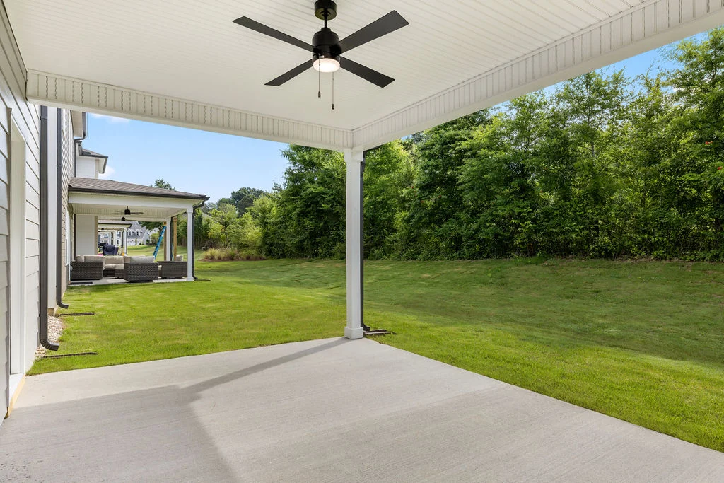 Covered patio with a ceiling fan overlooks a lush lawn and trees, adjacent to patio furniture. Built by Pratt Home Builders in Chattanooga TN.