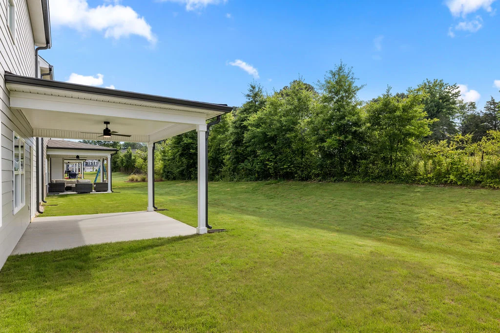 Spacious backyard with a covered patio by Pratt Home Builders in Chattanooga, TN. Lush green lawn bordered by trees under a clear blue sky.