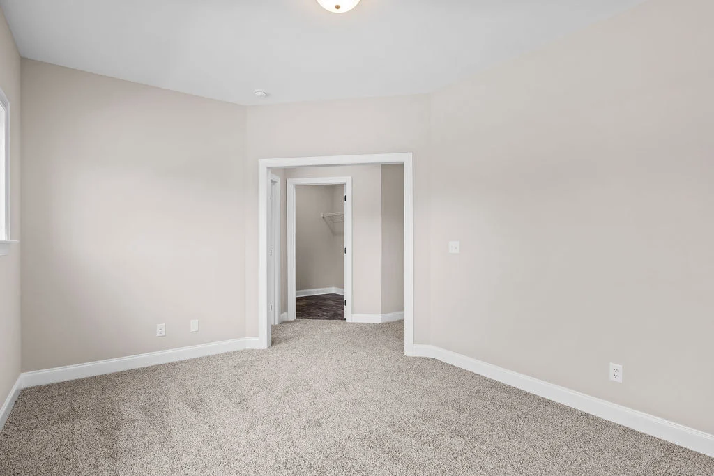 Empty room with beige walls, gray carpet, and a small hallway leading to a closet. Built by Pratt Home Builders in Chattanooga TN.