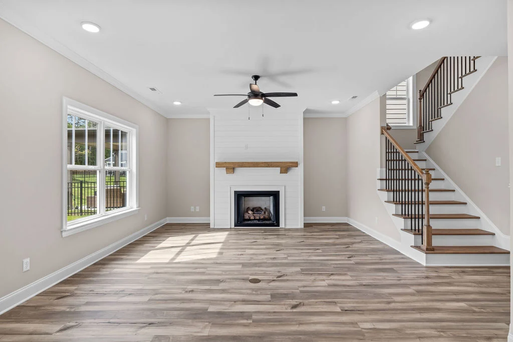 Spacious living room with light wood flooring, a fireplace, ceiling fan, and stairs. Built by Pratt Home Builders in Chattanooga TN.