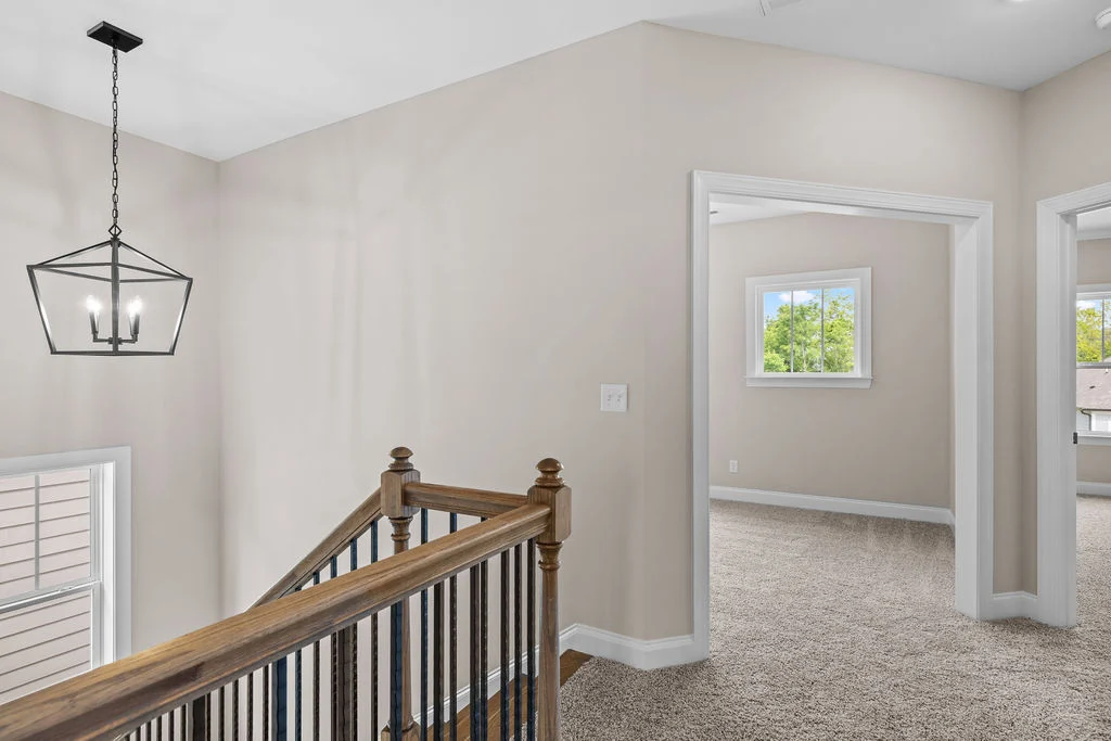 Modern hallway with wooden railing, light fixture, and doorways to carpeted rooms by Pratt Home Builders in Chattanooga TN.