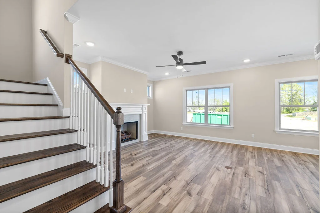 New Home Chattanooga TN. Living room by Pratt Home Builders, features light wood floors, white fireplace, large windows, and staircase with dark railings.