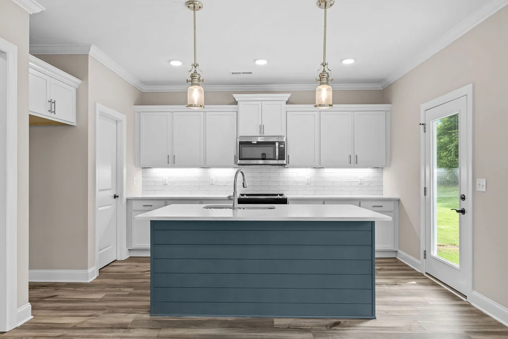 Modern kitchen designed by Pratt Home Builders in Chattanooga TN; features white cabinets, blue island, pendant lighting, and wood flooring.