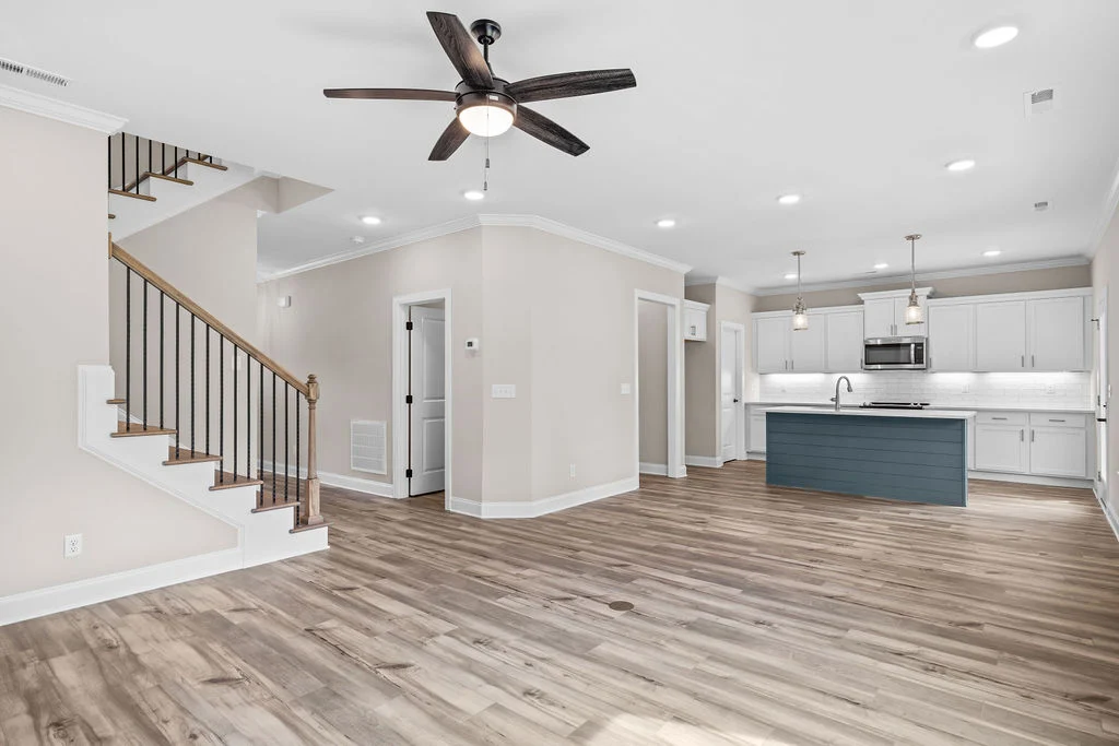 Modern open-concept kitchen and living area by Pratt Home Builders in Chattanooga TN, featuring hardwood floors, white cabinets, and a blue island.