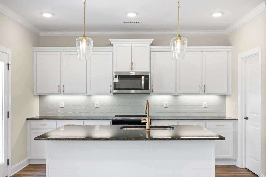 New home Chattanooga TN. Elegant kitchen with white cabinets, dark countertops, gold fixtures, pendant lights; designed by Pratt Home Builders.