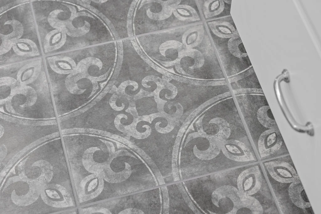 Ornate gray tile flooring with swirling patterns next to white cabinet. Featured in Pratt Home Builders in Chattanooga TN.