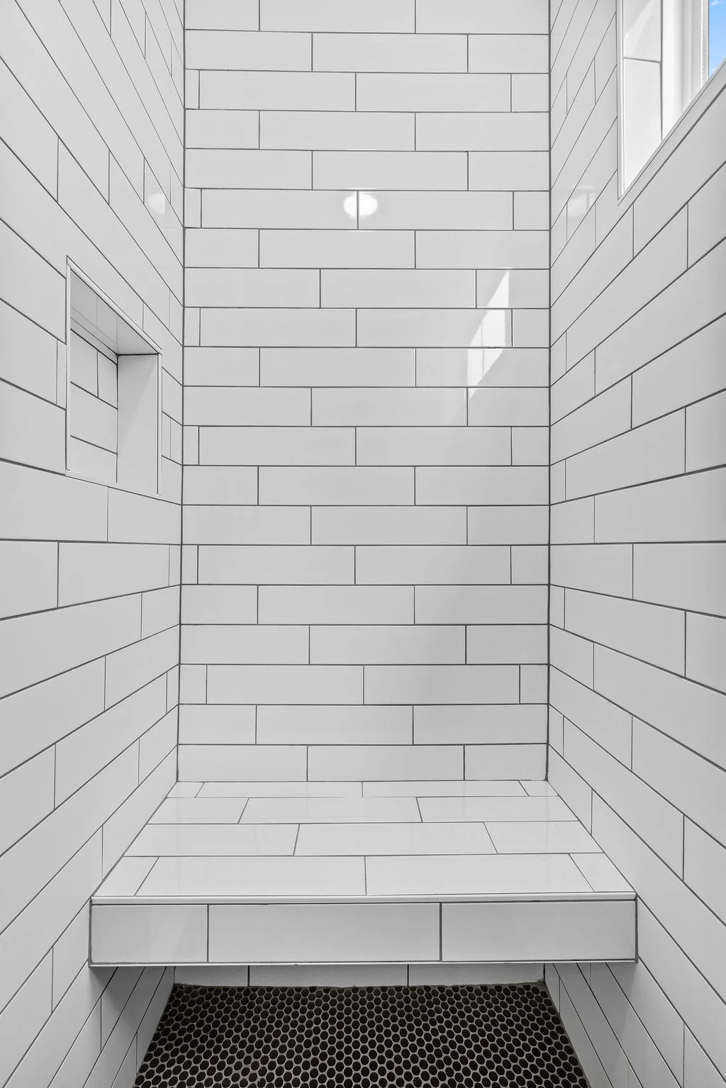 White tiled shower with built-in niche and bench, designed by Pratt Home Builders in Chattanooga TN.