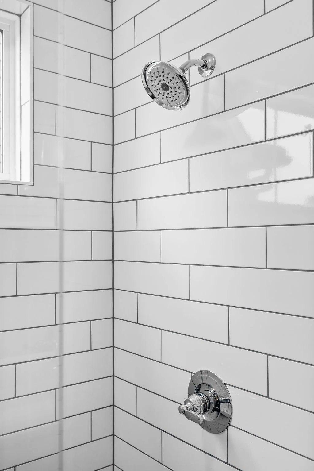 Modern shower with chrome fixtures, white subway tiles, and a small window by Pratt Home Builders in Chattanooga TN.