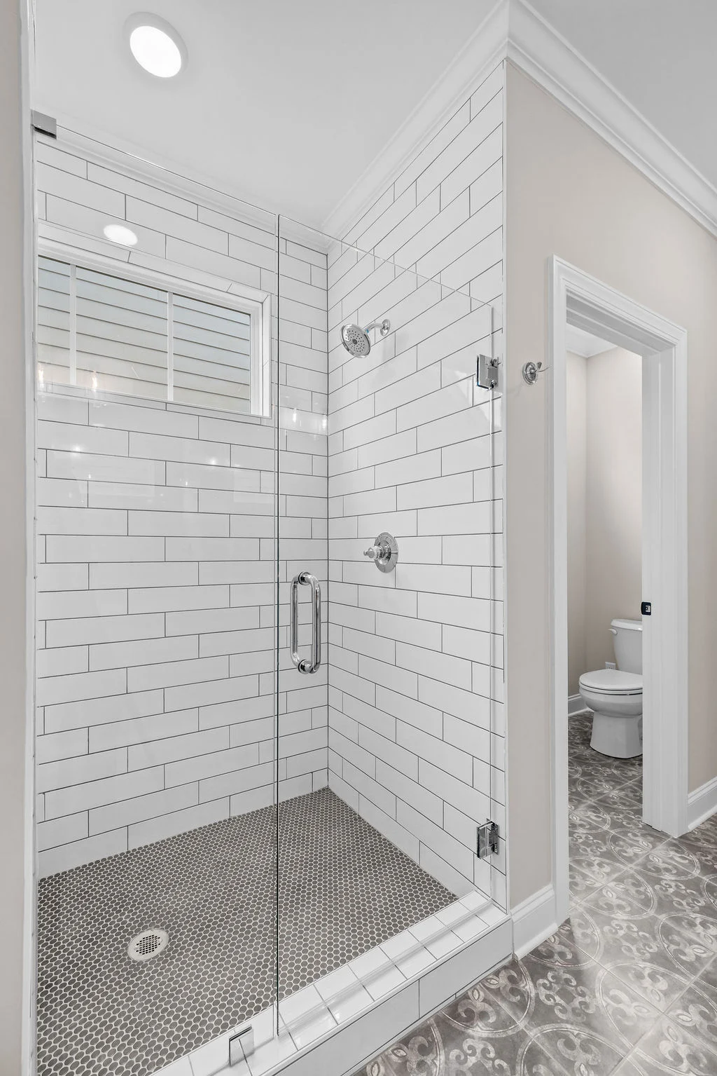 Modern bathroom with white subway tile shower, glass door, and patterned floor; designed by Pratt Home Builders in Chattanooga TN.