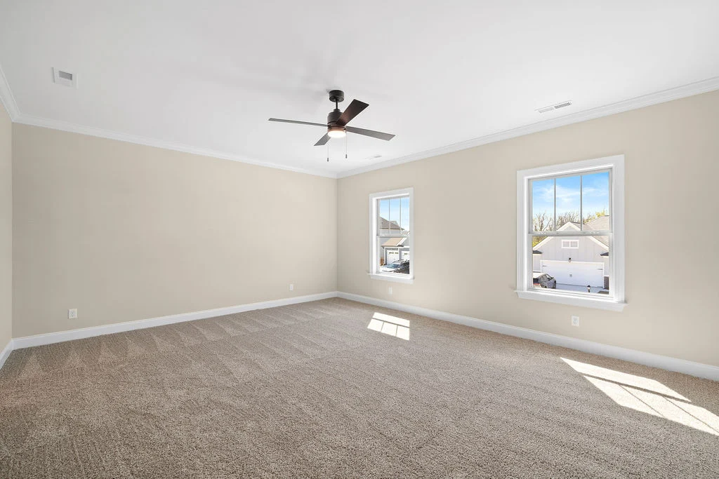 New Home Chattanooga TN. Spacious empty room with beige walls, carpeted floor, large windows, and ceiling fan. Crafted by Pratt Home Builders.