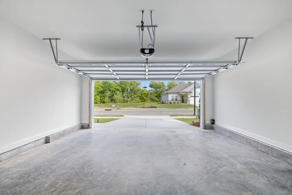Spacious garage interior by Pratt Home Builders in Chattanooga, TN, with open door revealing greenery and neighboring house.