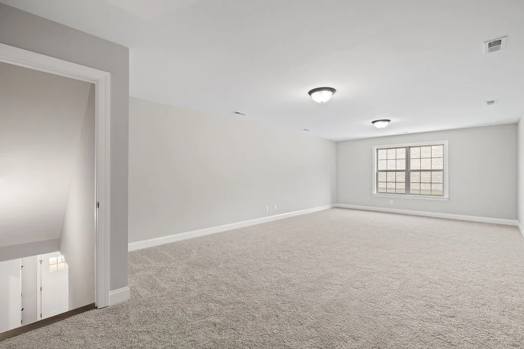 New Home Chattanooga TN. Spacious carpeted room with neutral walls, ceiling lights, and double window. Stairway visible; designed by Pratt Home Builders.