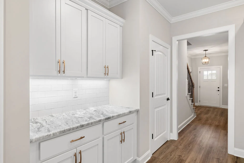 New Home Chattanooga TN. Elegant hallway with white cabinetry, marble countertop, and wood flooring by Pratt Home Builders, leading to a front door.