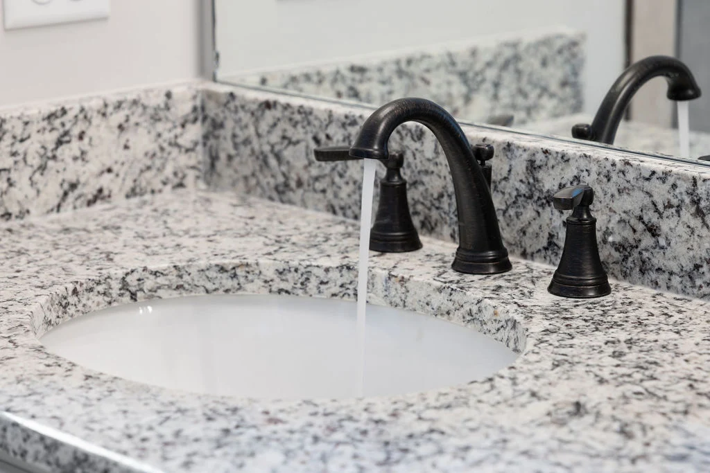 New Home Chattanooga TN. Granite bathroom counter with flowing water from a dark faucet. Design by Pratt Home Builders.