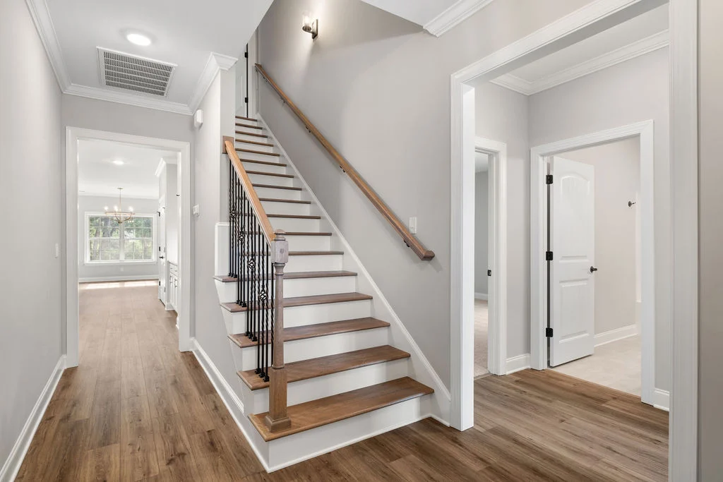 New Home Chattanooga TN. Modern hallway with wooden stairs, light gray walls, and a glimpse of a living area. Built by Pratt Home Builders.