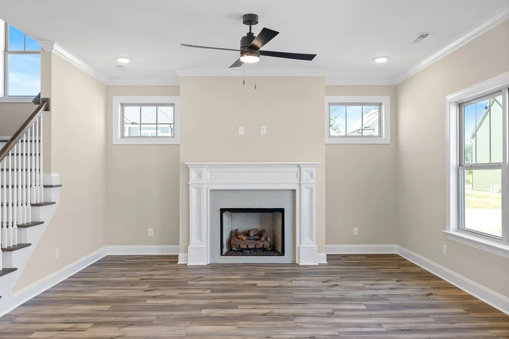 New Home Chattanooga TN. Bright living room with fireplace and ceiling fan, wooden floors and large windows, designed by Pratt Home Builders.